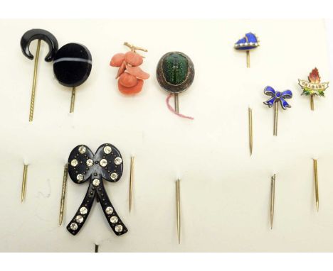 A collection of tie pins, including: a carved coral pin of floral design; a scarab beetle inset pin; a banded agate pin; some