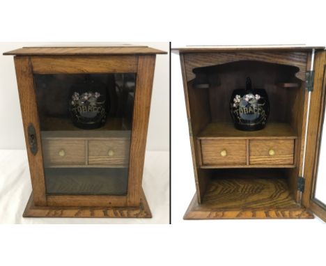 An oak smokers cabinet with glass panel door. 2 internal drawers, pipe racks and shelf. Complete with ceramic tobacco jar (a/