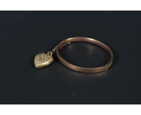 A 9ct rose gold bangle with engraved detail (dented) with a 9ct gold back and front heart shaped locket