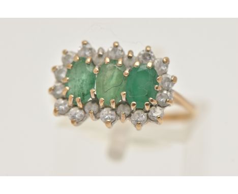 A 9CT GOLD EMERALD CLUSTER RING, designed as three oval cut emeralds each in a claw setting, within a surround of circular cu
