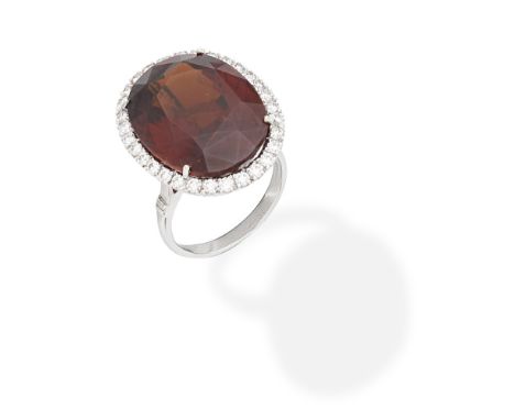 GARNET AND DIAMOND RINGThe oval-cut garnet within a brilliant-cut diamond surround, mounted in 18 carat white gold, maker's m