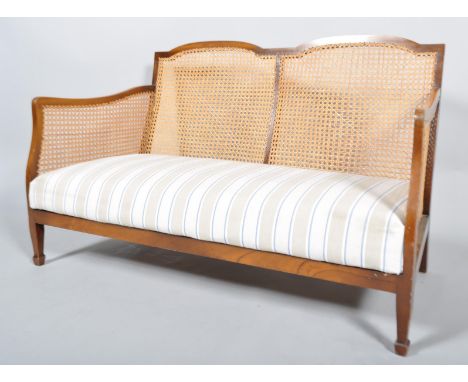 An Edwardian mahogany single cane bergere two seat sofa with caned back and arm and upholstered seat, on spindle forelegs, 77