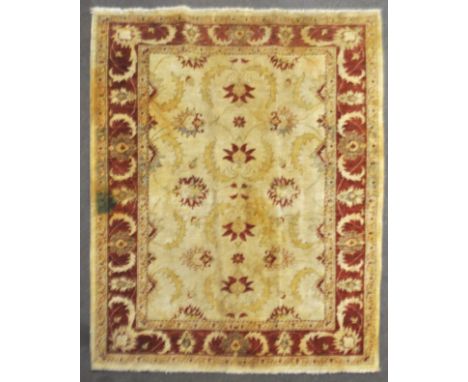 A wool carpet with beige ground woven with scrolling leaves and flowerheads in yellow, red and blue, within a dark red foliat