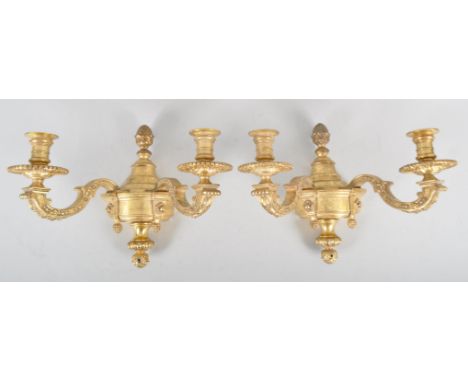 A pair of 20th century brass double wall sconce candlestick electric lights, in the Regence style, cast with husks to each s-