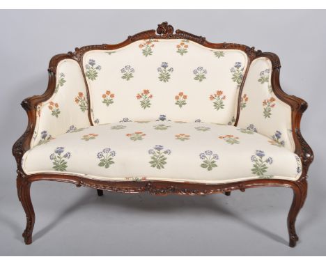 A late Victorian mahogany two seat sofa, the frame carved overall with scrolls and swags, upholstered in floral embroidered f