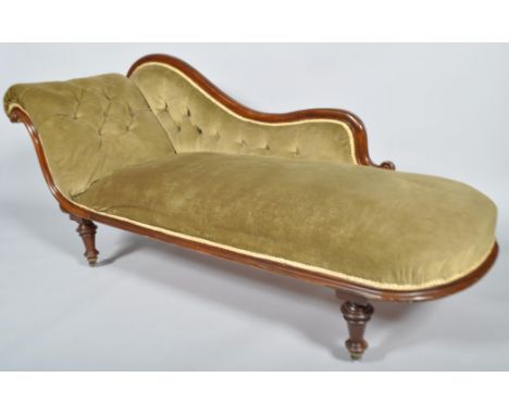 A 19th century mahogany chaise longue having carved strolled decoration, button back green upholstery, all raised on turned l