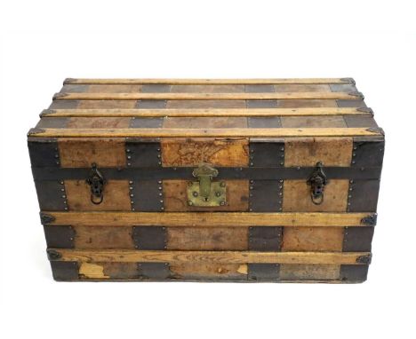 An Edwardian bound pine travelling trunk, with varnished splat mounts and studded straps, opening to reveal a vacant interior