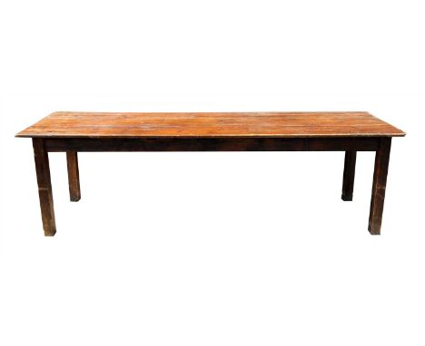 A large rustic stained pine kitchen table the long planked top above a plain frieze raised on squared legs 77cm high, 265cm l