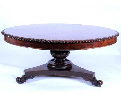 A large Victorian plumb pudding veneered dining table, of circular form, the top with a carved fluted border above a cross-ba