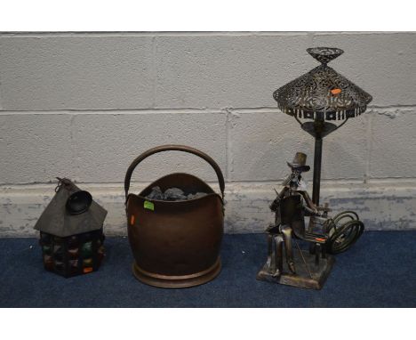 A FIGURAL METAL TABLE LAMP, of a seated man reading a book, along with a brass coal bucket containing coal and a hanging lant