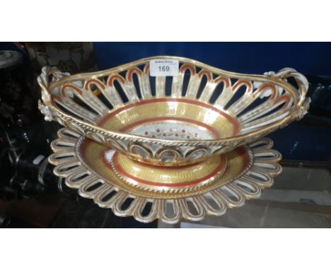 An early 19th century ceramic basket with pierced gilt decorated border, on a similarly decorated stand with griffin head arm
