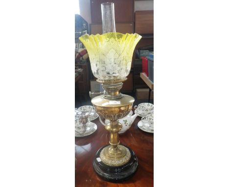 An early 20th century brass oil lamp with black ceramic foot and original yellow frosted shade  