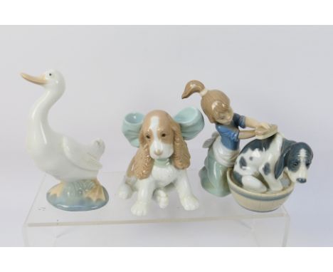 A Lladro figure group, # 5455 Bashful Bather, depicting a young girl washing a dog and two Nao animal figures, dog and goose,