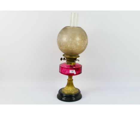 A Victorian brass oil lamp with cranberry glass font, font 15 cm (d), approximately 55 cm (h) to top of chimney. [W]