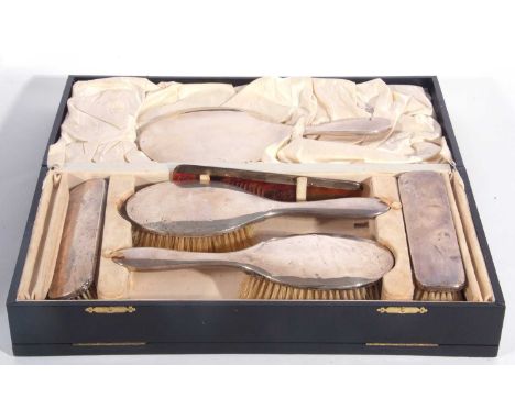 A cased dressing table set, comprising hand mirror, two hairbrushes, two clothes brushes and a framed comb of plain polished 