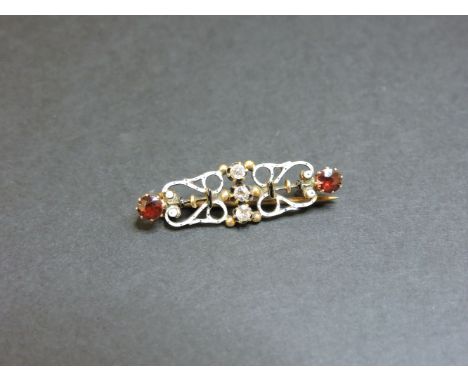 A gold diamond and garnet scrolled bar brooch, with white and black enamel decoration
