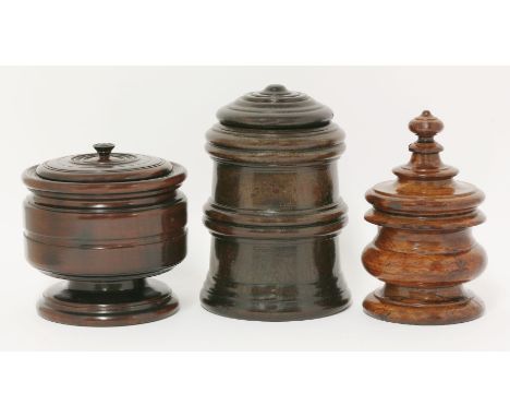 Three turned treen boxes and covers,the first in walnut with removable finial revealing a small hole, 18cm high,the second, p