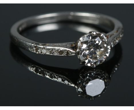 A platinum and diamond ring. The larger stone flanked by diamond set shoulders. Size L 1/2. 2.91g.  