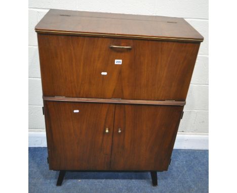 A MID-CENTURY TOLA AND BLACK WALNUT COCKTAIL CABINET, with an articulated door, that’s enclosing a glass shelf and a mirror b