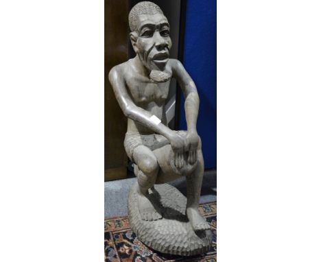 African figure, modelled as a tribesman, playing a drum, 92cm.