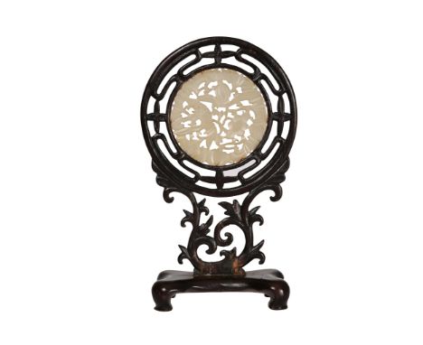 A Chinese carved jade plaque pendant, the carved and pierced hardwood stand enclosing a pierced circular jade plaque carved w