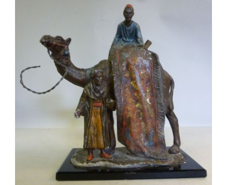 An early 20thC painted spelter novelty table lighter, fashioned as an Egyptian camel and two Arab carpet sellers, on a cerami