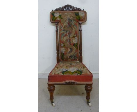 A mid Victorian walnut showwood framed prie-dieu, having a scroll carved crest, turned, fluted supports, a floral tapestry up