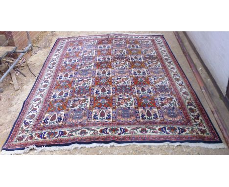 A Turkish carpet with repeated panels of flowers and trees on a red, blue and cream coloured ground  115'' x 76''