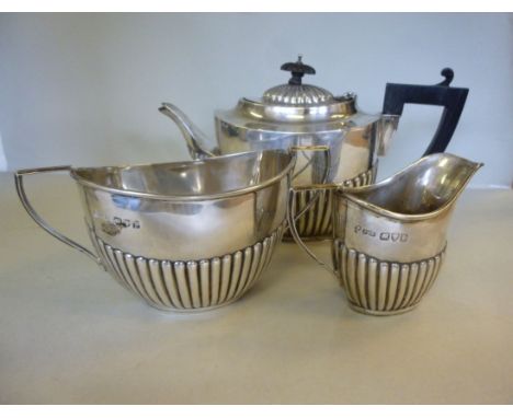 A late Victorian three piece silver tea set of oval demi reeded form, the teapot with an ebonised handle, a sugar basin and m