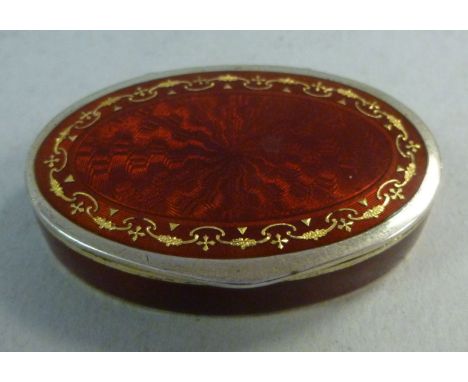 An early 20thC Continental silver coloured metal pill box of oval form, having a hinged lid with engine turned red enamel dec