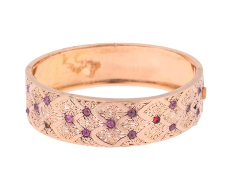 A French 18ct gold ruby hinged bangle, set with round cabochon rubies with pierced floral decoration, French assay mark, band