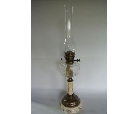 A Victorian oil lamp raised on a ceramic foot and stem with foliate decoration, with moulded clear glass fount set beneath a 