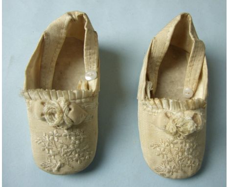 A pair of Victorian baby shoes of ivory gross grain, embroidered with flowers with silk ribbon trim, 11.6cm long.