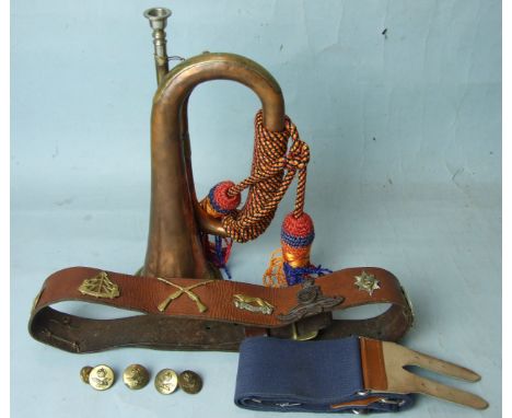A copper and brass bugle with silk cord and tassels, a leather belt with eight cap badges and other items.