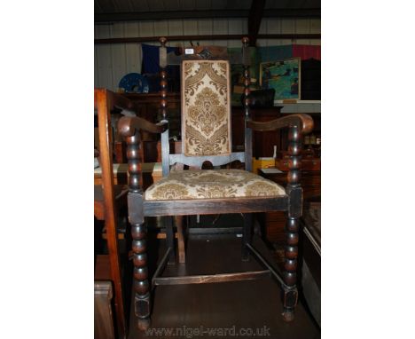 A 1920's Oak Carver Chair with finial back and shaped and carved top rail over a padded back, with scroll arms, bobbin turned