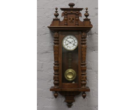 A carved mahogany cased 8 day wall clock with Roman numeral markers and chiming on a coiled gong.