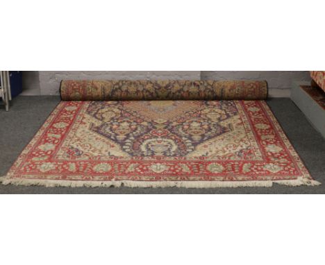 A Persian wool carpet, blue ground with a red border and having stylised flowers and urns, 310cm x 207cm.