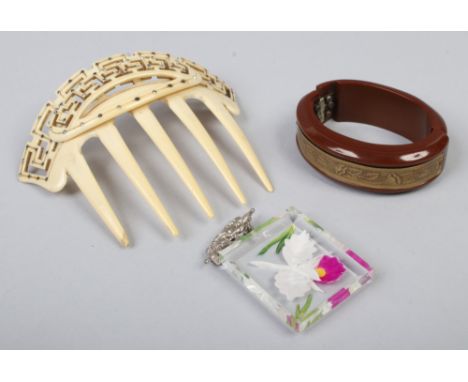 An early 20th century celluloid hair comb set with white paste stones, a Bakelite and gilt metal bangle and a pendant brooch 