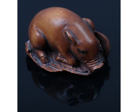 A fruitwood Netsuke formed as a recumbent pig with glass set eyes, signed.