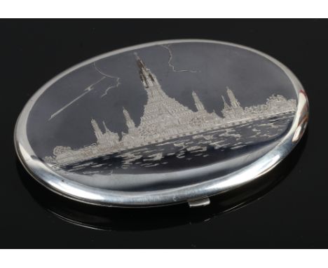 A sterling silver and niello powder compact, possibly Burmese with a deity to one side and temple to the other.
