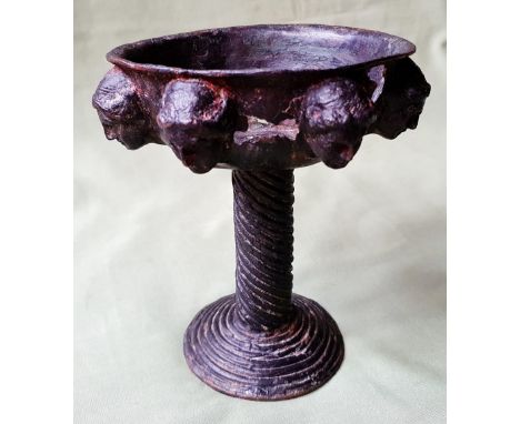 An unusual bronze pedestal cup, the sides of the bowl decorated with seven heads in full relief, 6" high