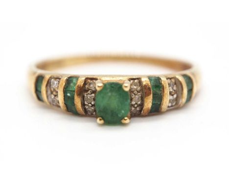 A 14ct emerald and diamond ring, set to centre with an oval faceted emerald in a four claw mount, with lightly tapered should