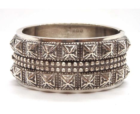 A late Victorian silver bangle, the upper half of the hinged bangle with raised decoration, the lower half plain, 3mm wide, i