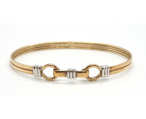 A 9ct bi-colour bangle, the oval bangle with loop terminations and hinged clasp, stamped 375 with London assay mark, inner di