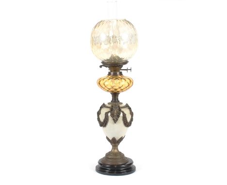 A pottery and brass mounted baluster table oil lamp, having applied ram's head masks, garland and ribbon decoration, amber gl