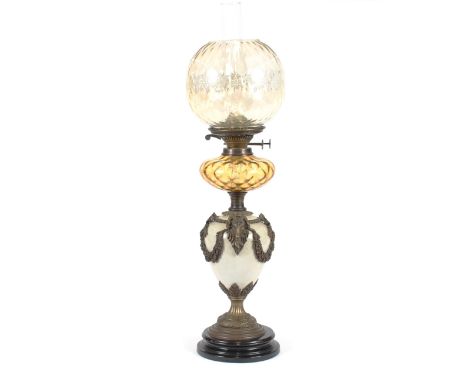 A pottery and brass mounted baluster table oil lamp, having applied ram's head masks, garland and ribbon decoration, amber gl