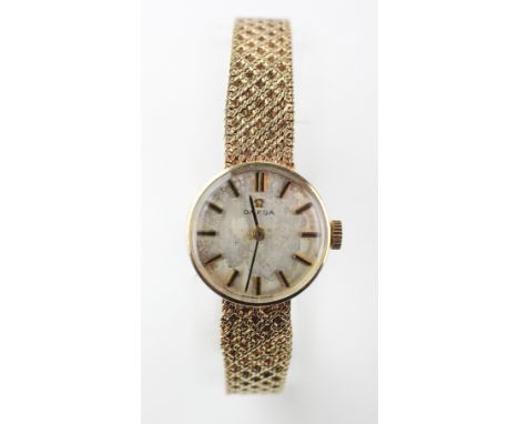 A yellow gold Omega wristwatch. Circular silver dial with baton markings. Integrated weaved bracelet with fold over clasp and