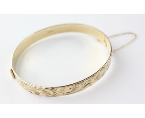 A yellow metal half engraved hinged bangle with slide clasp and safety chain. Hallmarked 9ct gold, Birmingham, 1989 15.5 gram