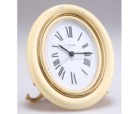 CARTIER: A GILT METAL AND ENAMEL TRAVEL ALARM CLOCK, oval, with white dial and Roman numerals, within a cream enamel border, 