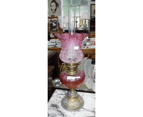 AN EDWARDIAN OIL LAMP, with a cranberry reservoir on a brass base, with a frosted cranberry shade 20" high (including chimney